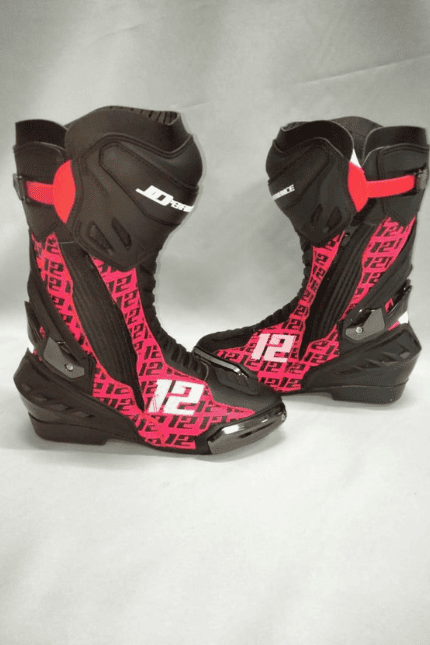 A pair of black and pink LeMieux motorcycle boots with white number 12 graphics, displayed on a light gray fabric background.