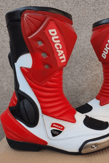 A pair of red, white, and black Ducati motorcycle boots for the motorcycle riders with the brand name 'DUCATI' prominently visible on the red protective plates.