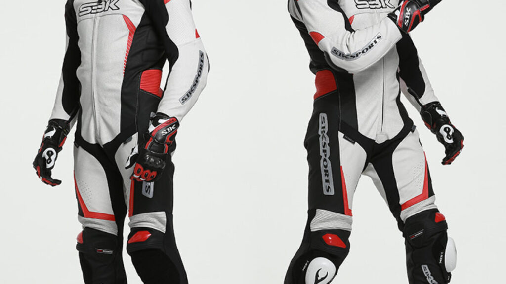 A motorcyclist showcases a sleek black, red, and white racing suit with protective gloves, posing confidently against a light background.