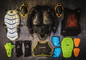An array of protective motorcycle gear, including body armor, knee guards, chest protectors, and impact pads, laid out on a textured surface.