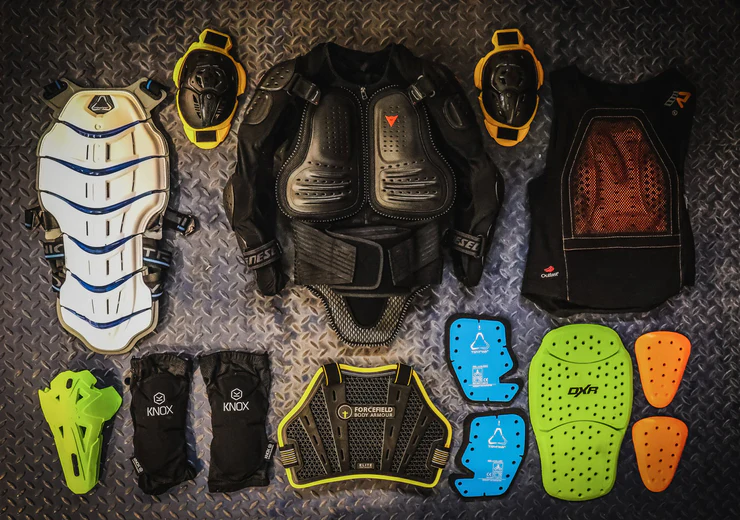 An array of protective motorcycle gear, including body armor, knee guards, chest protectors, and impact pads, laid out on a textured surface.