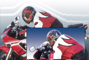 A motorcyclist in a red and white leather suit and helmet rides a red sportbike, focusing intently on the road ahead.