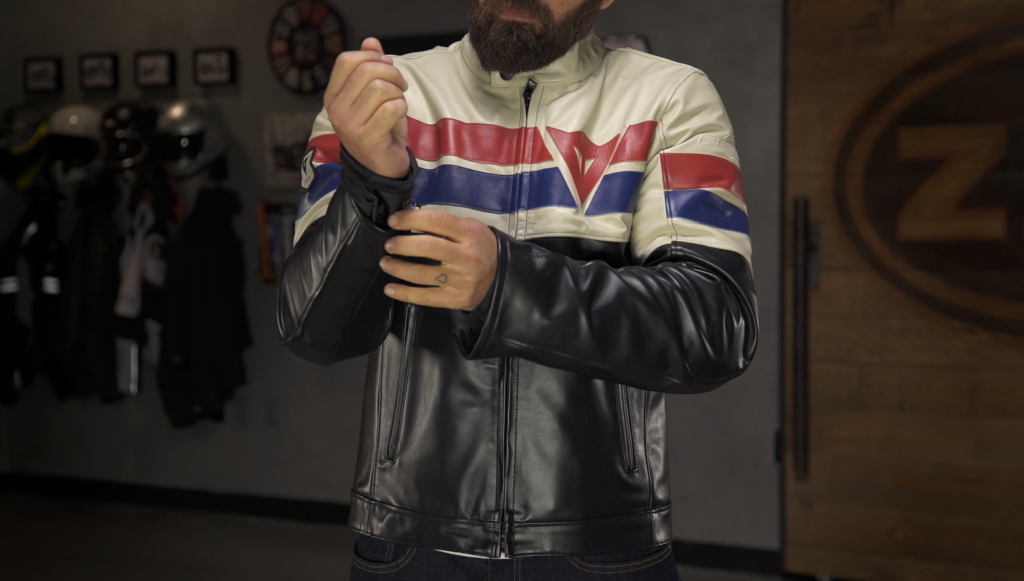 A man adjusts the cuff of a vintage-style motorcycle leather jacket, featuring bold red, white, and blue stripes.