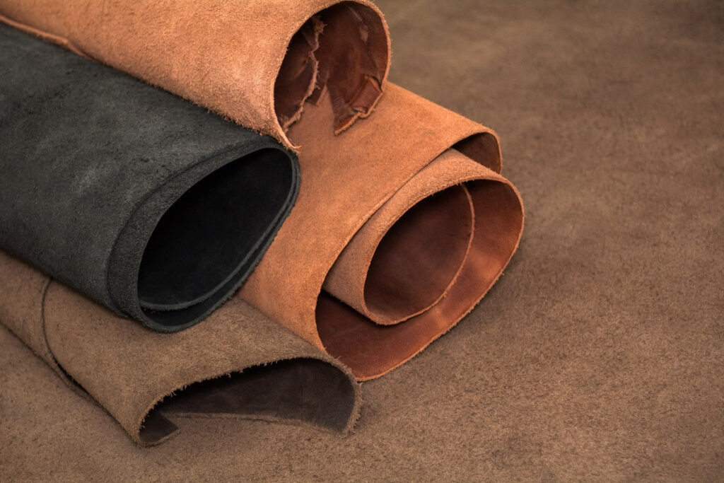 A collection of rolled-up suede leather in various colors, including black, brown, and tan, resting on a textured background.
